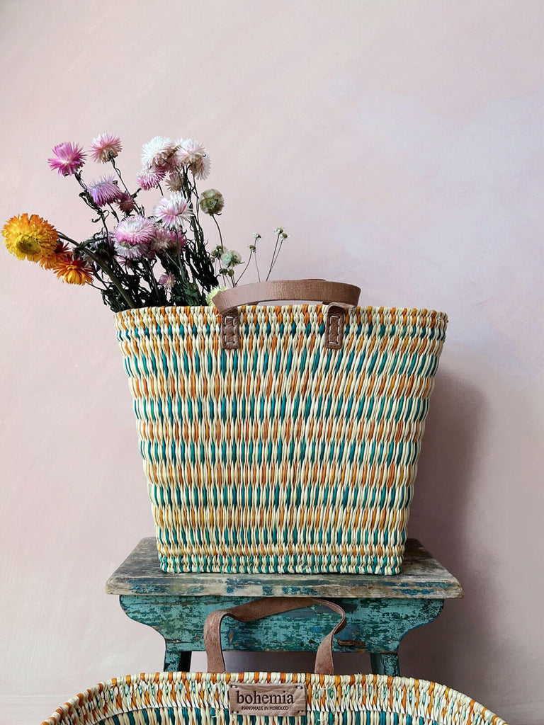 Colourful woven reed shopper basket with teal and orange pattern, leather handles and bunch of dried flowers