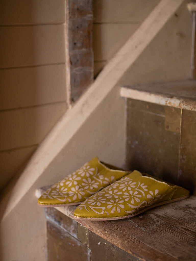 A pair of mustard leather, daisy patterned pointed babouche slippers on a rustic staircase 