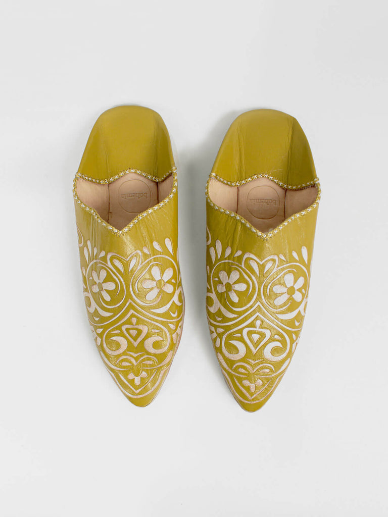 A pair of mustard pointed leather slippers with decorative arabesque heart pattern.