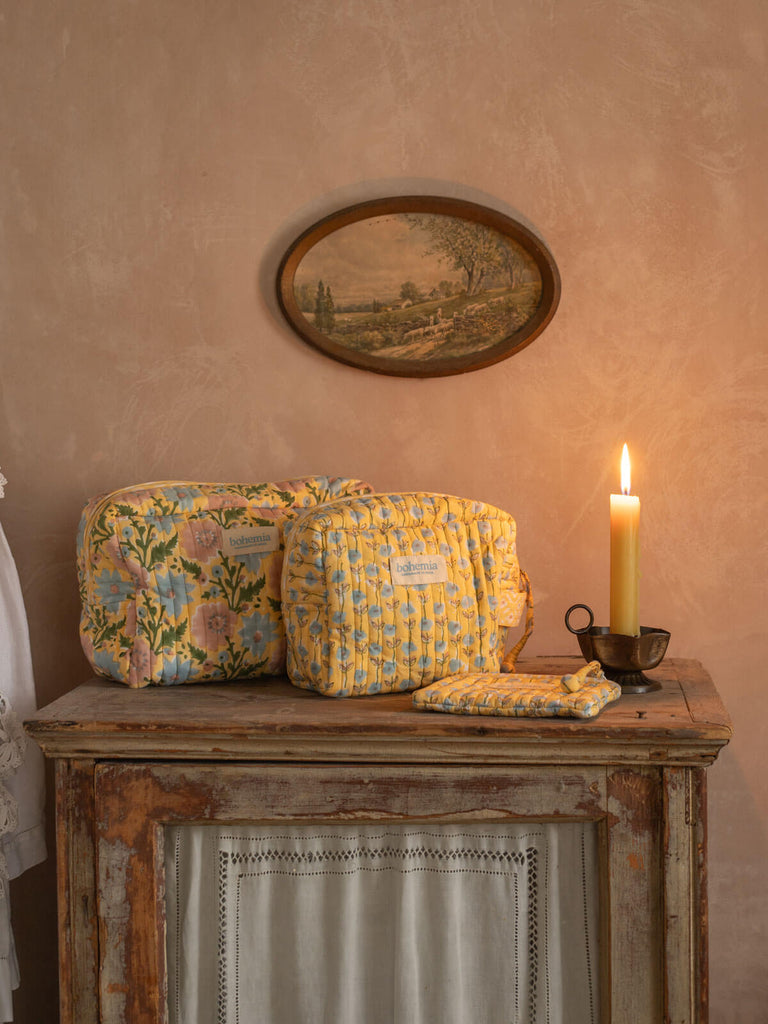 Quilted floral print washbags in yellow and blue on a antique cupboard with lit candle