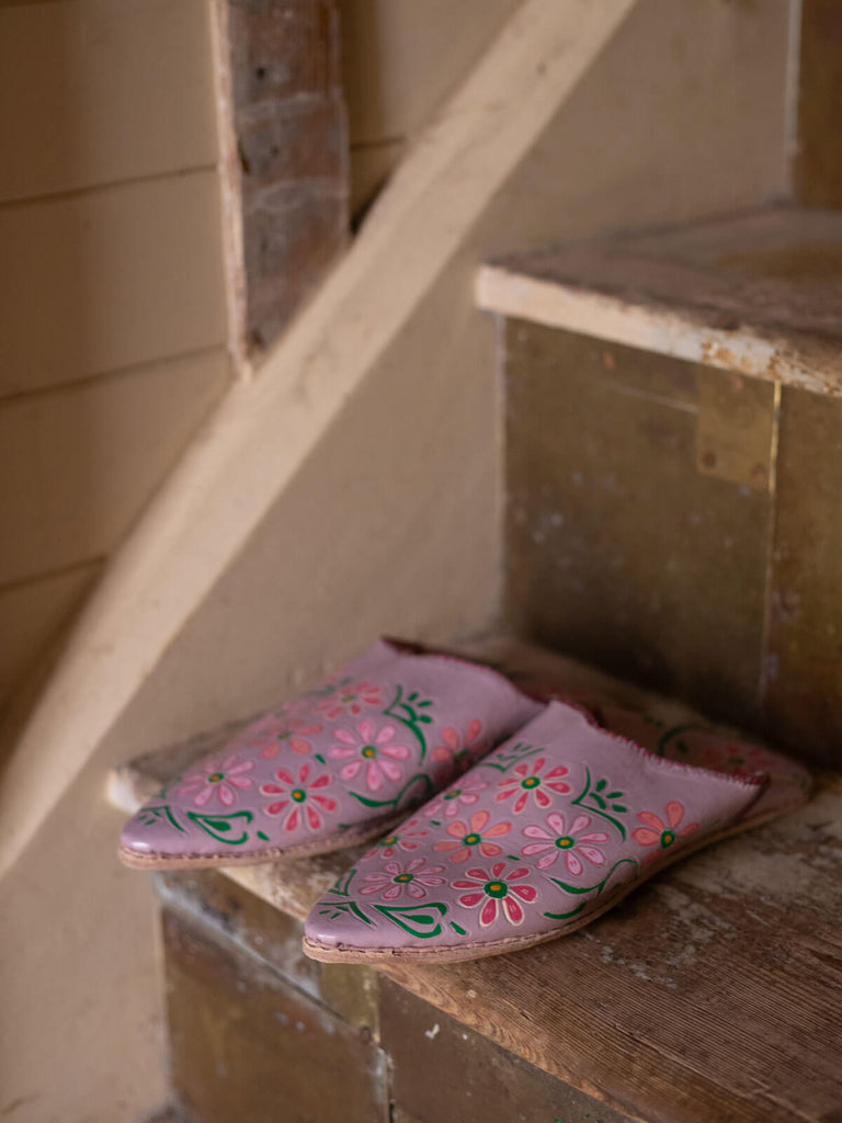 Hand painted babouche slippers with floral lilac pattern on a rustic wooden staircase