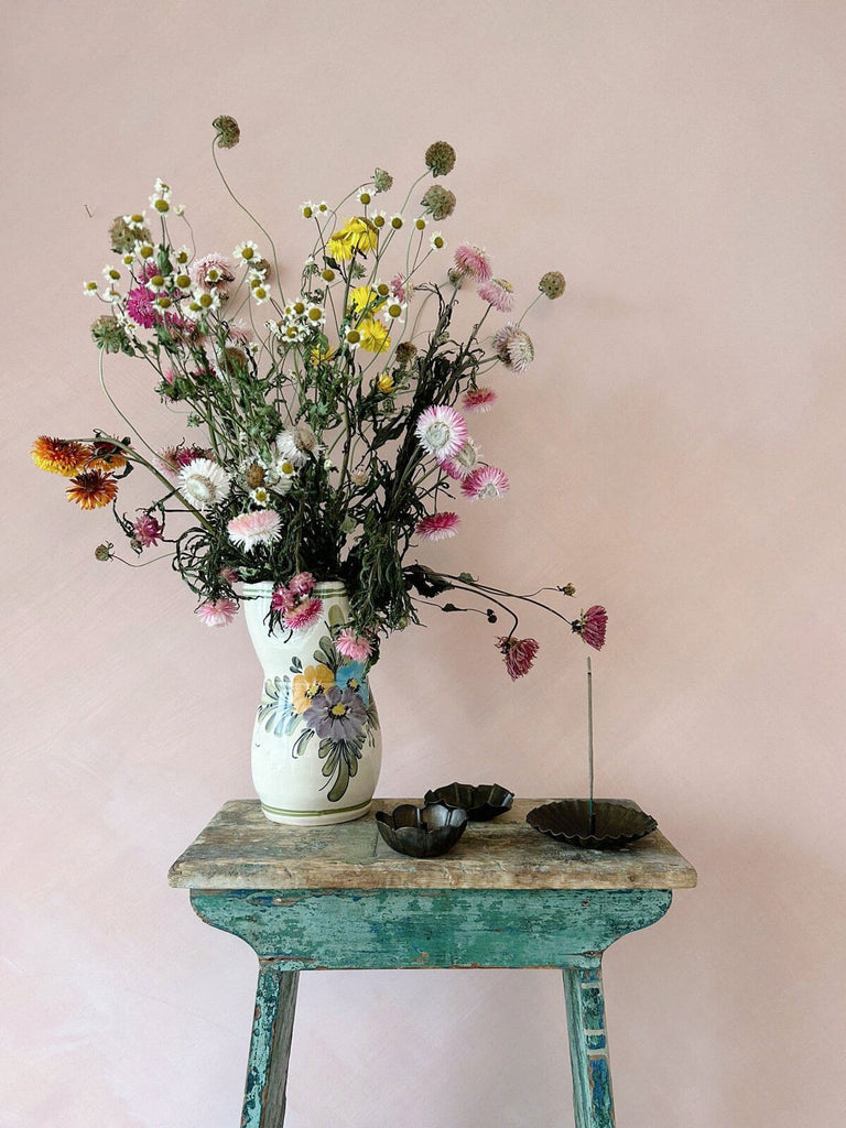 Three antiqued metal incense holders on a table with vase of dried flowers