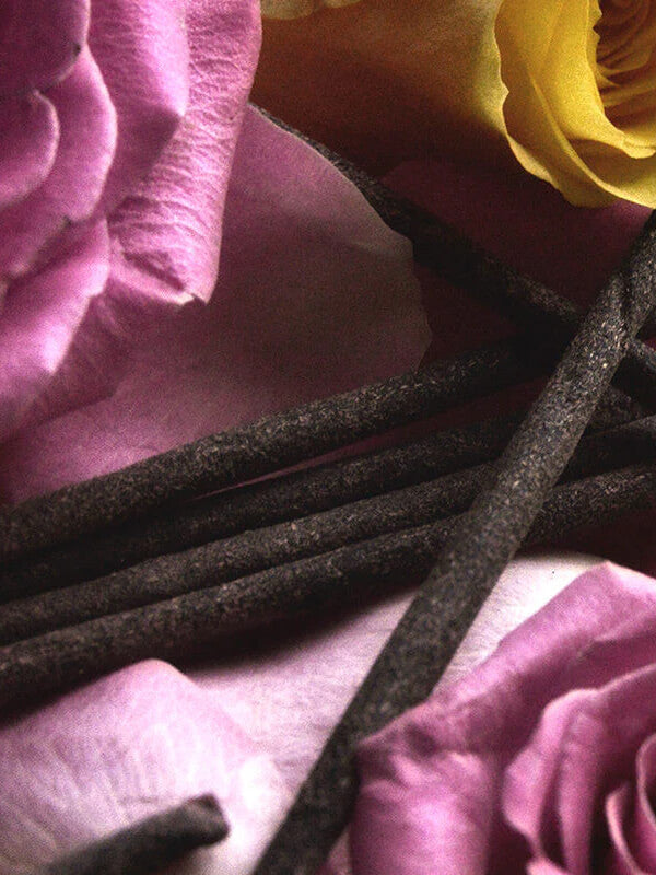 Incense sticks surrounded by pink and yellow roses