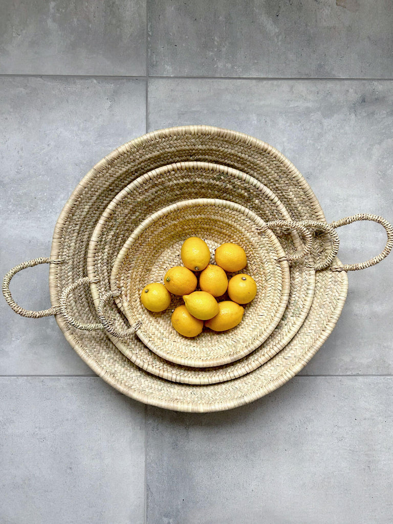 Small, medium and large Moroccan woven plates with handles nesting together holding lemons