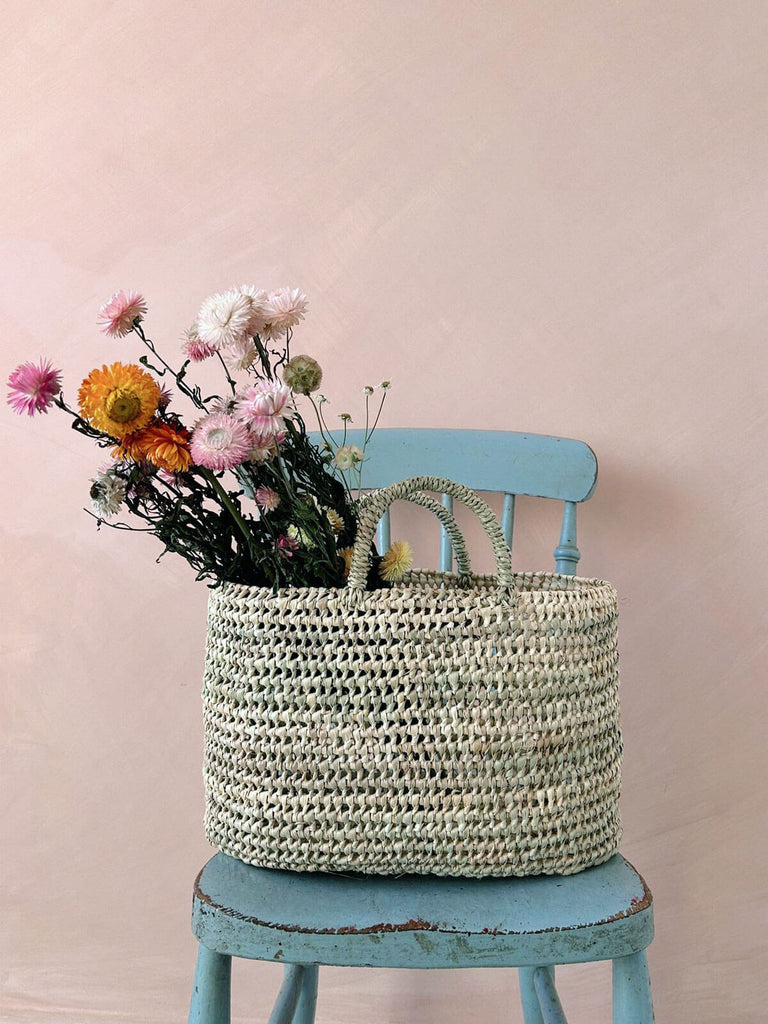 Natural woven straw nesting basket with dried flowers on a blue chair
