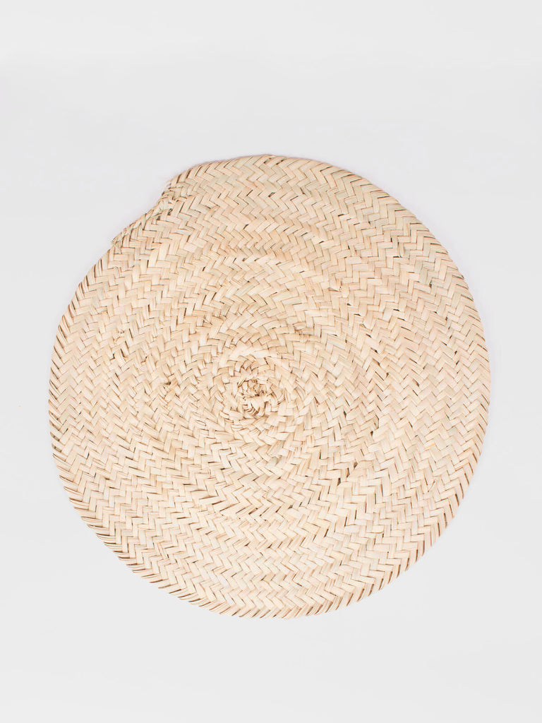 Simple, rustic, round placemat woven from natural palm leaf