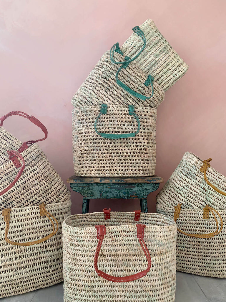 Different colours of the pleated leather handle baskets in front of a pink wall