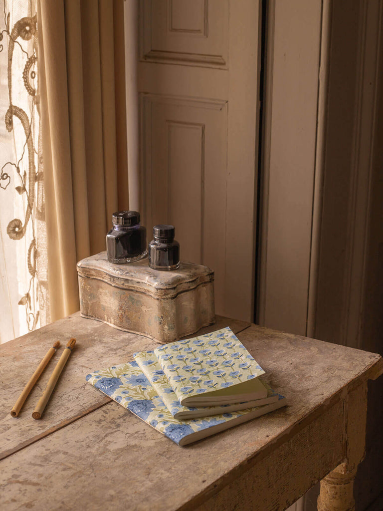 Three different sized sage green and blue notebooks on a antique desk with ink pots.