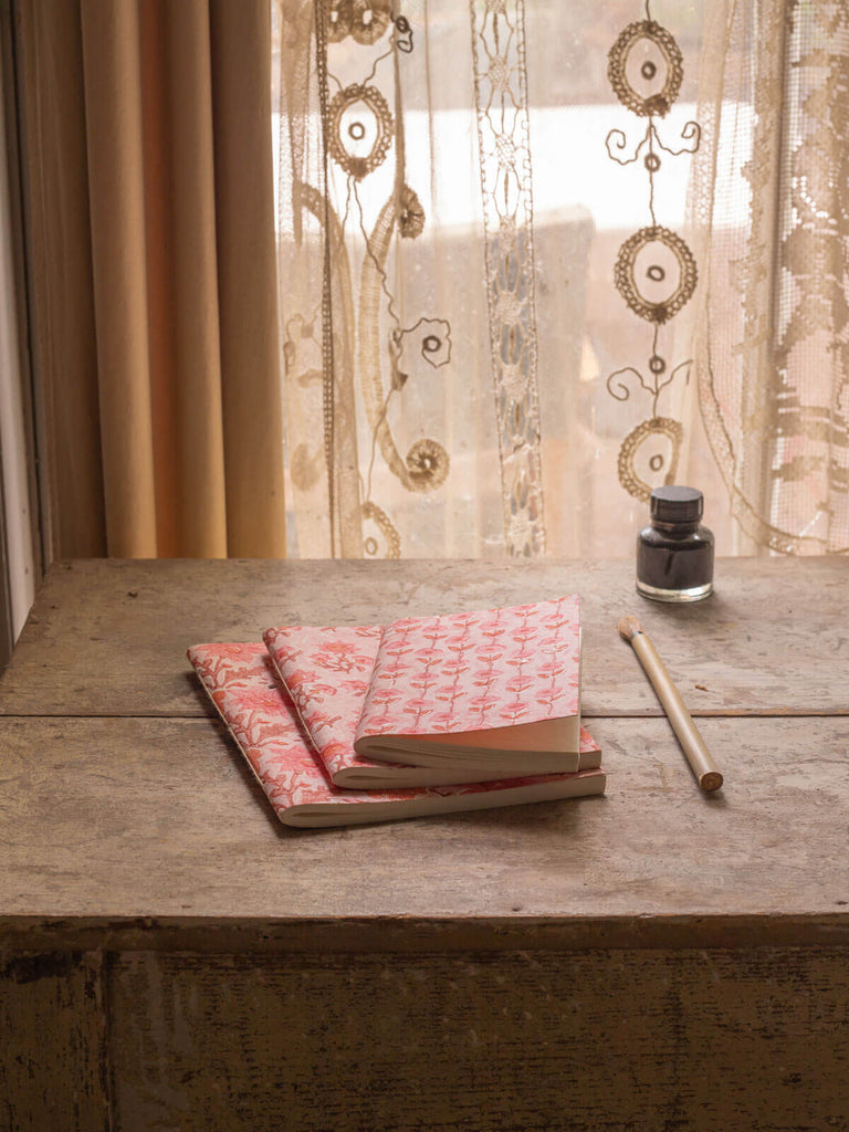 Three pink block printed notebooks of different sizes on a antique desk