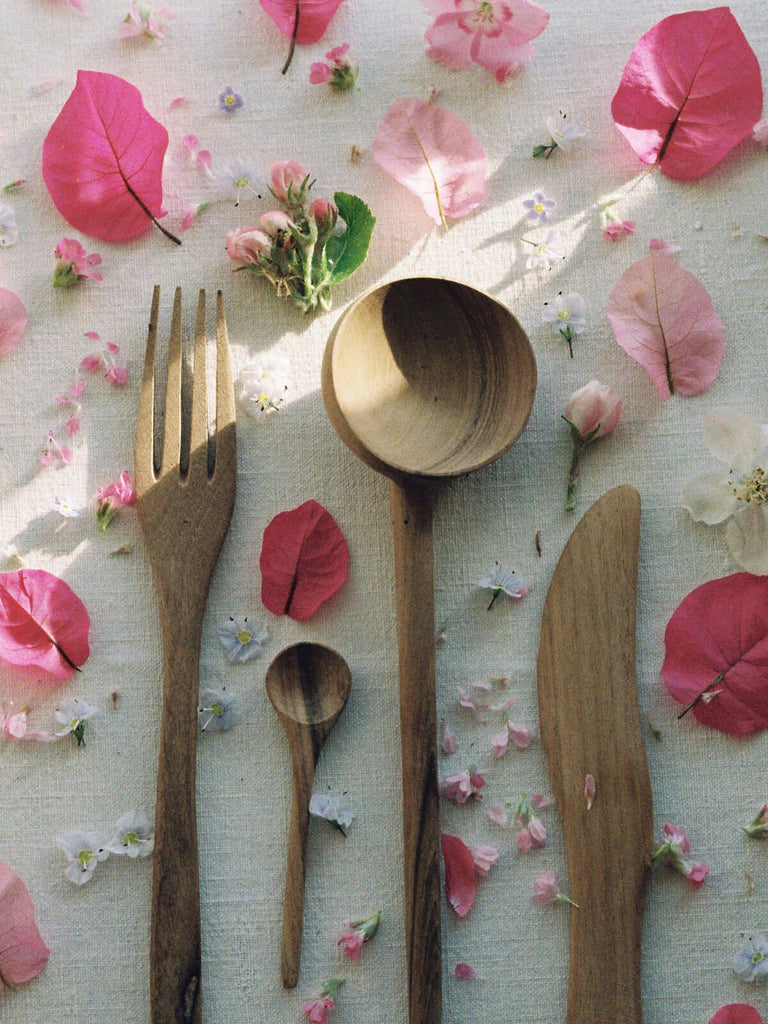 Walnut wood spoons, fork and knife on a linen tablecloth surrounded by pink petals