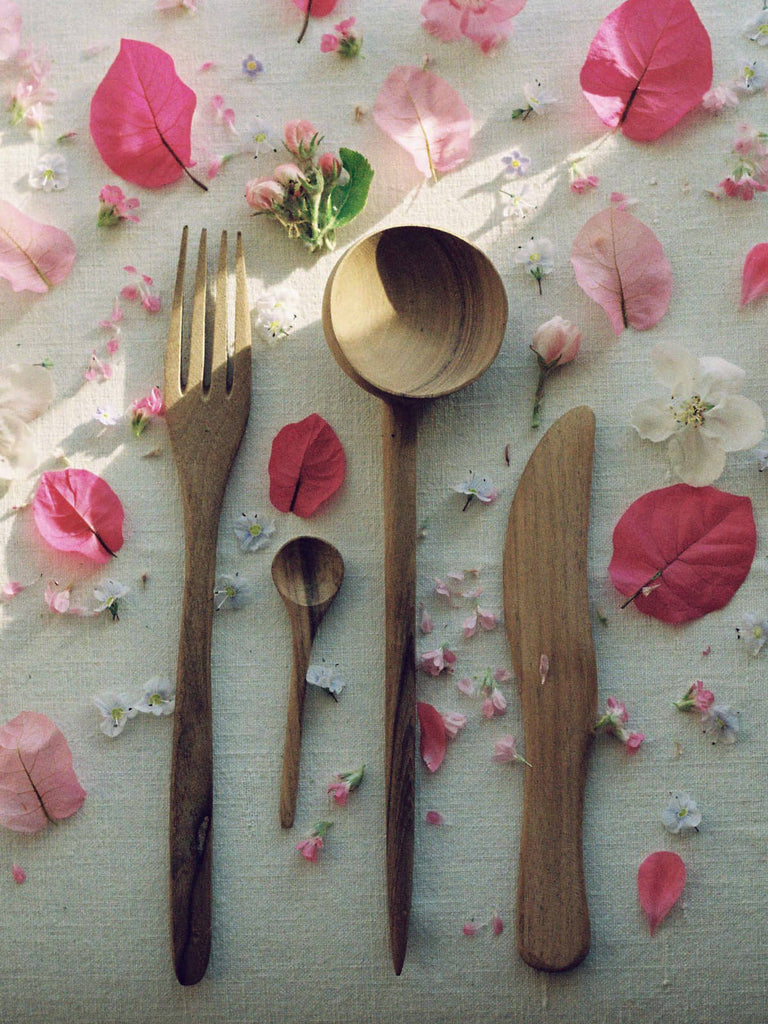 Walnut wood fork, spoons and knife on a linen tablecloth surrounded by pink flower petals