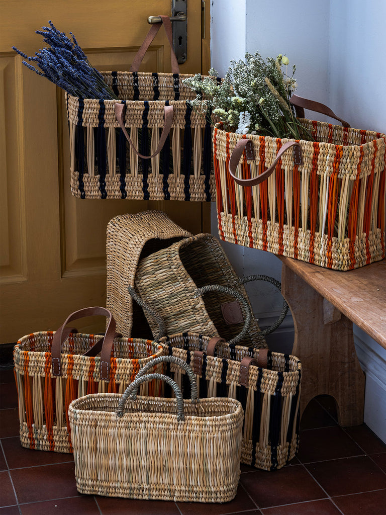 Natural woven reed basket bags in different colours in a hallway, handwoven by Moroccan artisans for Bohemia