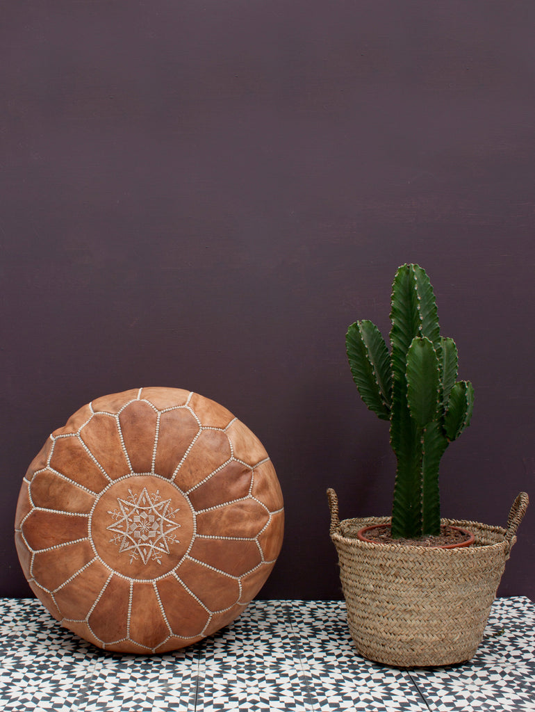 Moroccan Leather Pouffe in tan next to a basket holding a cactus