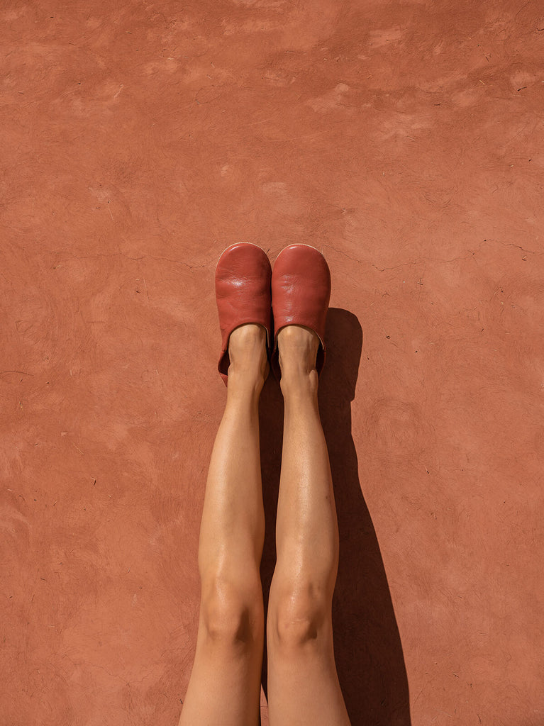 Model wearing Terracotta Moroccan babouche leather slippers by Bohemia Design against a terracotta wall