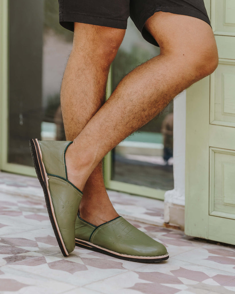 Moroccan berber babouche slippers in olive leather worn by model standing on terracotta tiles