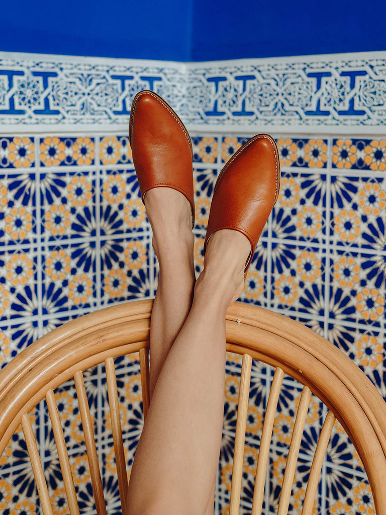Bohemia-leather-mules-tan-with-rattan-chair-and-blue-Moroccan-tiles