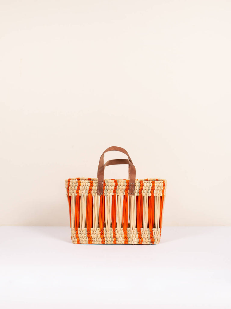 Small boxy woven basket bag with decorative orange stripe design and leather handles