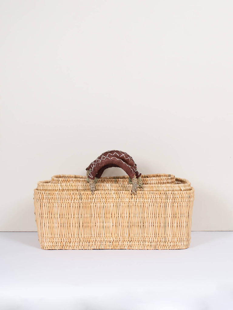 Set of three natural woven rectangular reed wicker nesting baskets with leather handles.