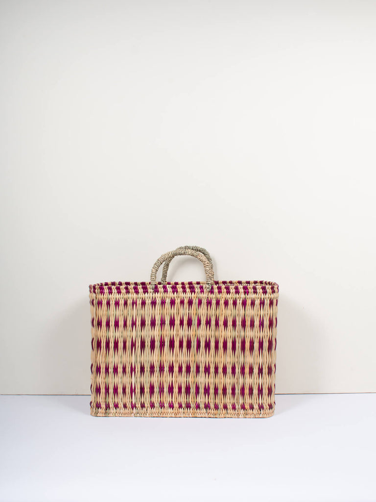 Natural woven reed basket bag with short handles and featuring a skillfully weaved violet pattern