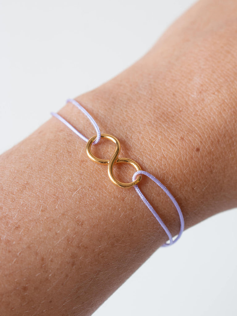 Woman wearing Gold and lilac silk thread friendship infinity bracelet by Bohemia Design