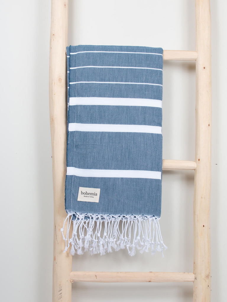 Ibiza Summer Hammam Towel in indigo stripe pattern by Bohemia Design hanging from a wooden ladder