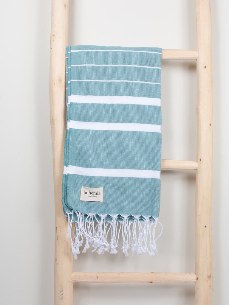 Ibiza Summer Hammam Towel in grey green stripe pattern by Bohemia Design hanging on a wooden ladder