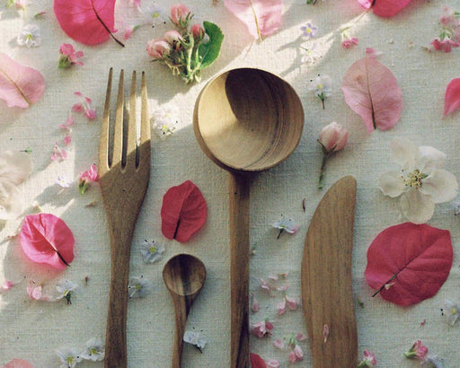 Handmade walnut wood fork, spoons and knife on a table with pink petals