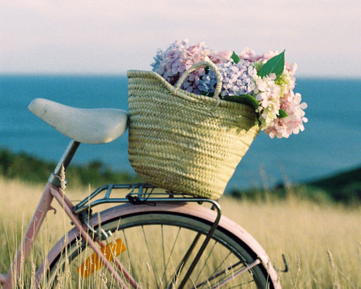 Natural woven shopping market basket filled with flowers on the back of a pink bicycle