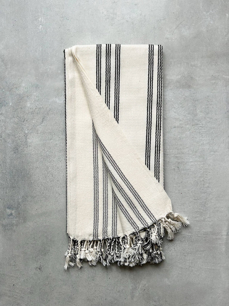 Soft cotton hammam towel with a ticking stripe in charcoal black, displayed on a grey textured background