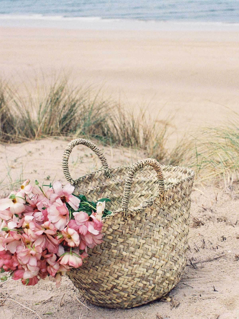 Bohemia natural woven Beldi Basket filled with pink flowers on a beach