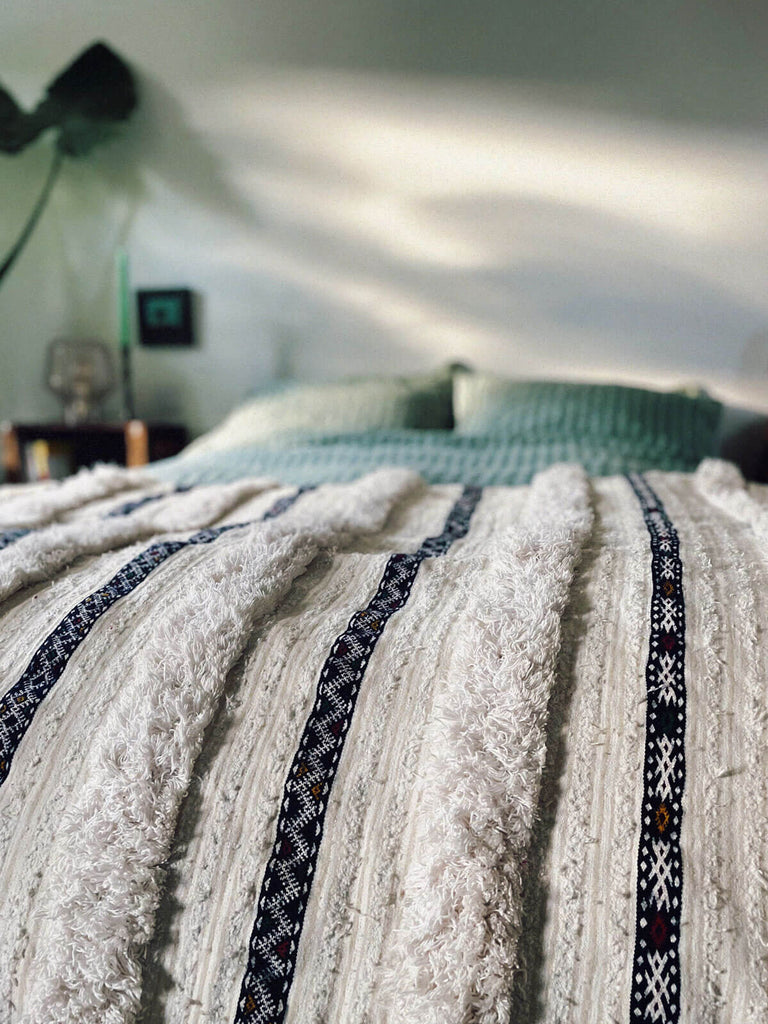 Close up of vintage handira blanket draped on a bed with green striped bedding