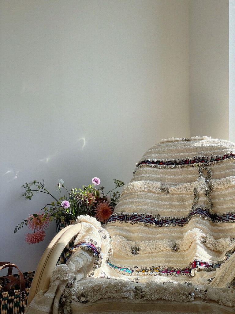 A traditional Moroccan Wedding Blanket draped on a chair features cream and white stripes and silver sequins.
