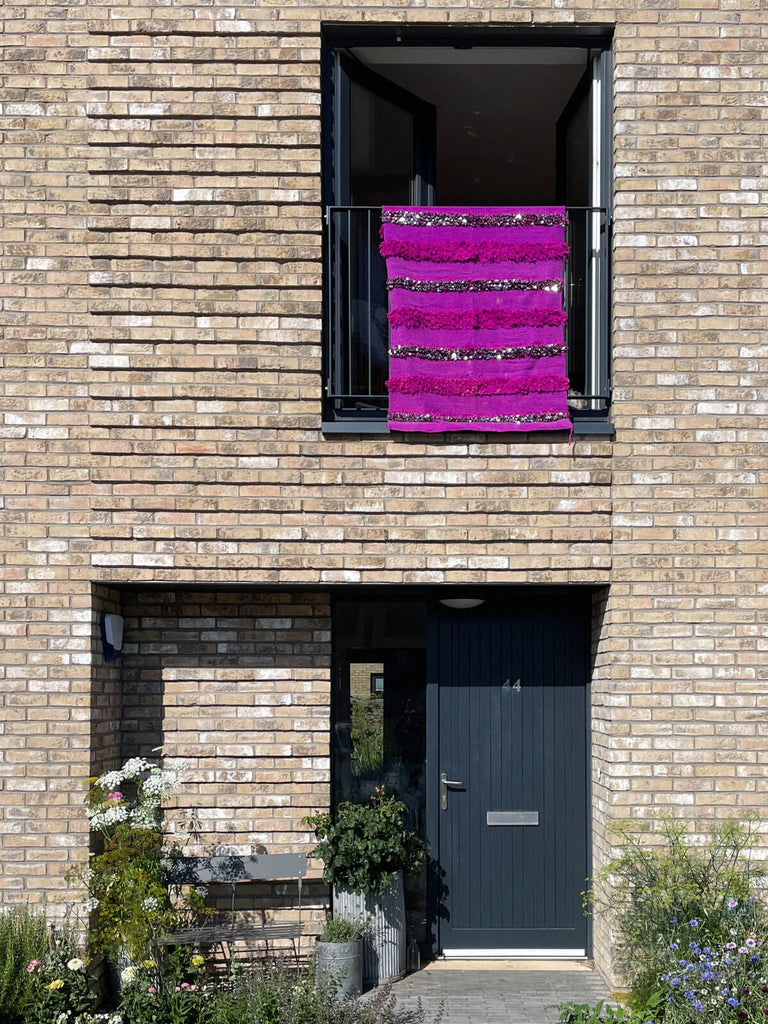 Bright pink handira blanket with rows of sparkling sequins hanging on a balcony of a modern house