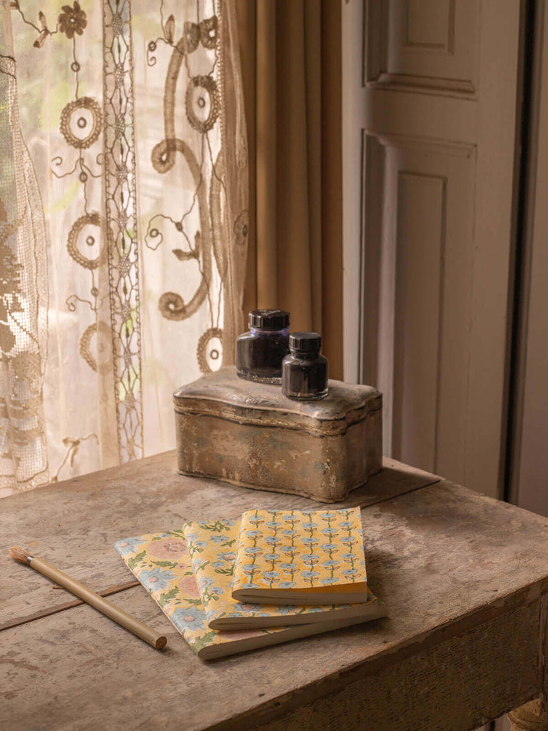 Three different block printed notebooks in buttermilk on a antique desk beside writing tools and ink pots
