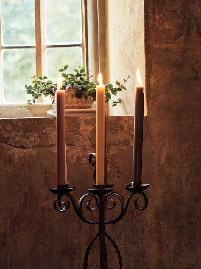 A trio of colourful lit True Grace candles in a rustic iron candleholder 