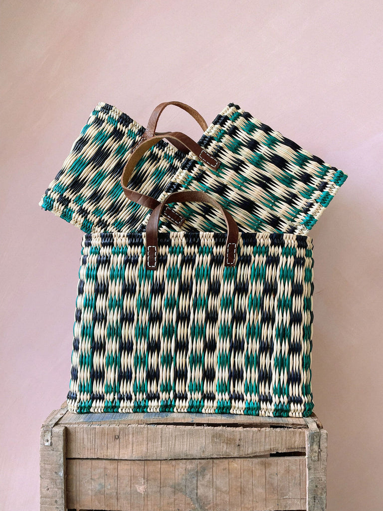 A stack of three different sizes of chequered woven reed basket bags in indigo and green