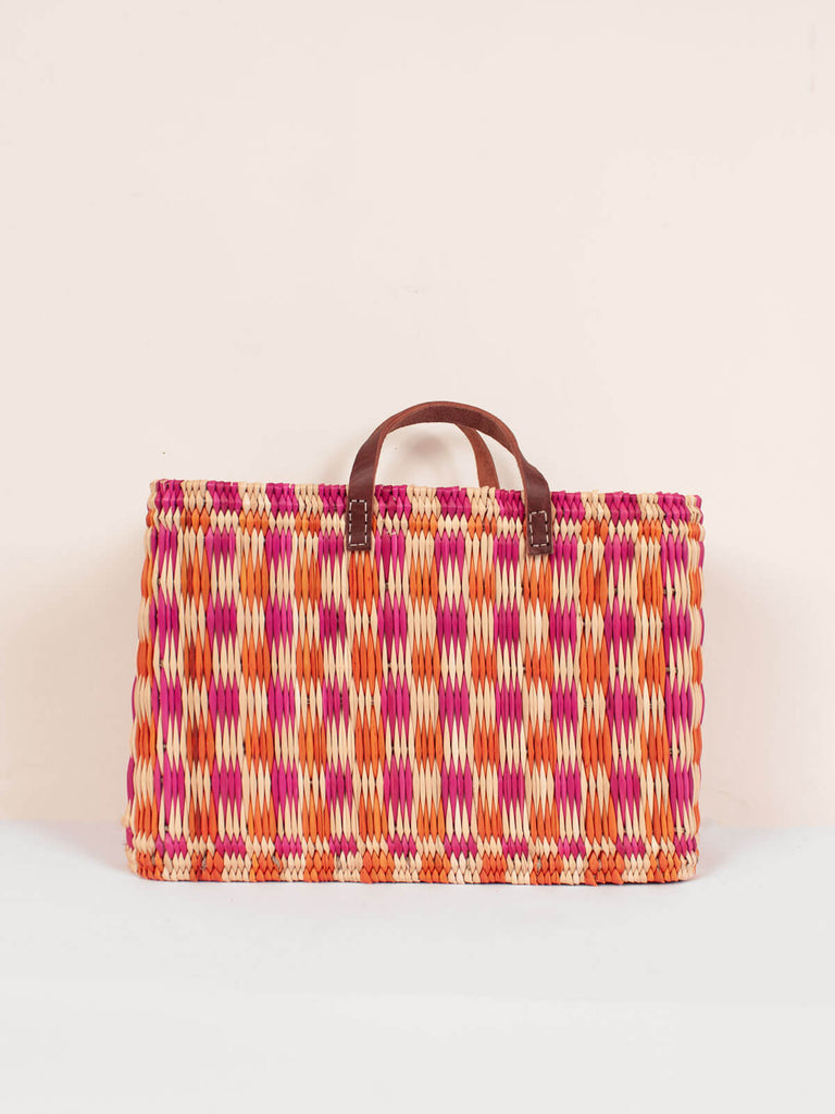 A large rectangular, pink and orange chequered woven basket bag with leather handles