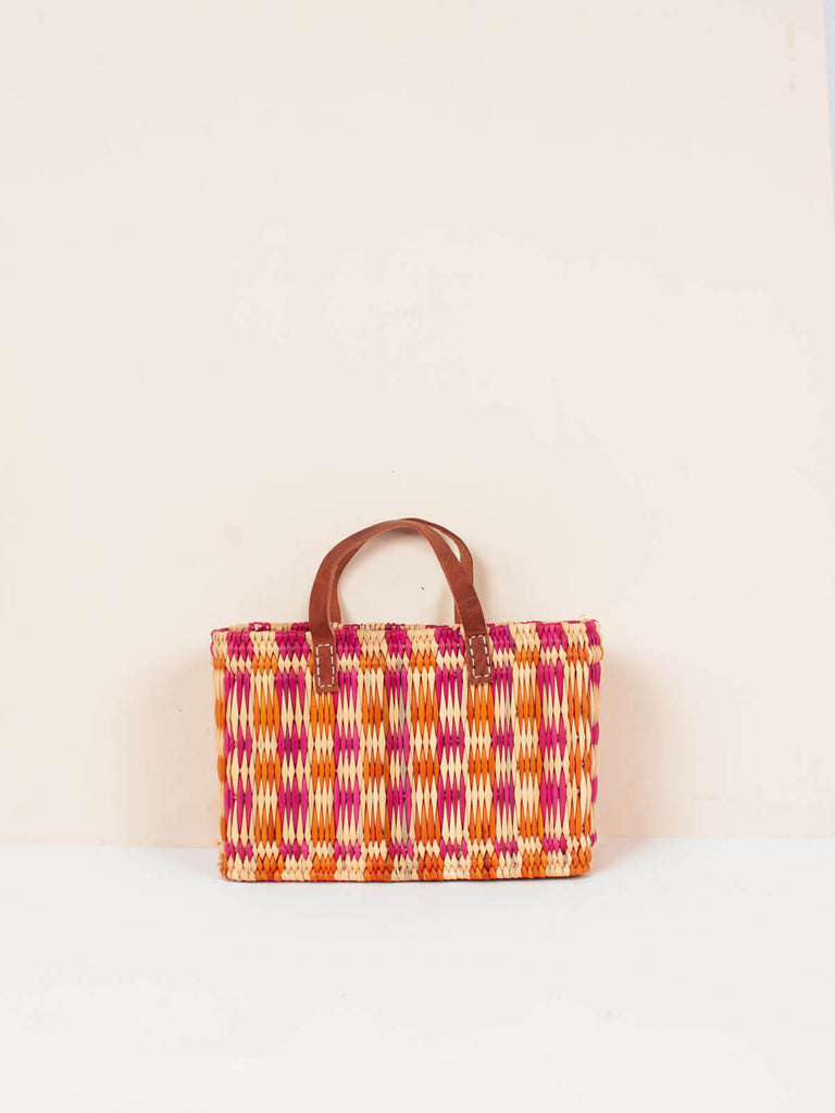 A small, boxy, rectangular, pink and orange chequered woven basket bag with leather handles