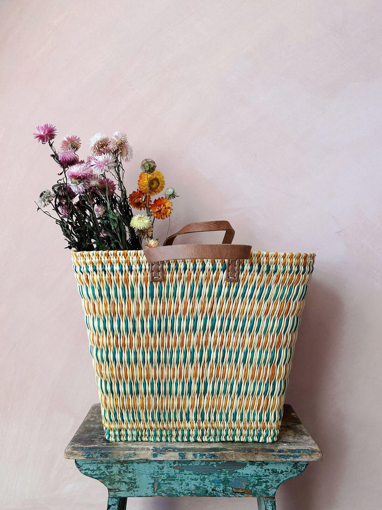 Tall colourful reed shopper basket with leather handles filled with dried flowers