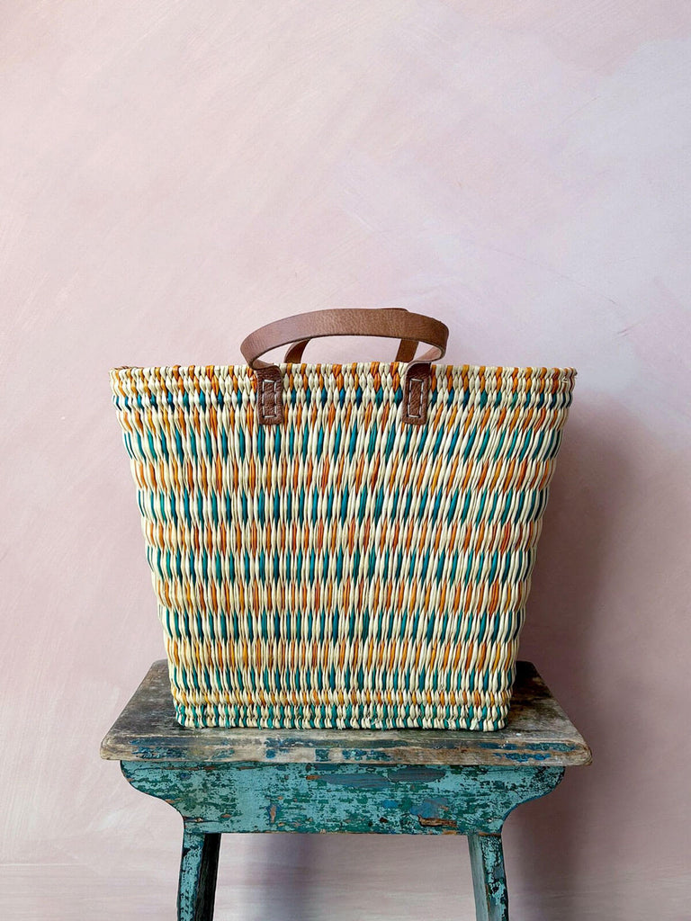 A colourful woven wicker reed basket with leather handles for market shopping or stylish home storage