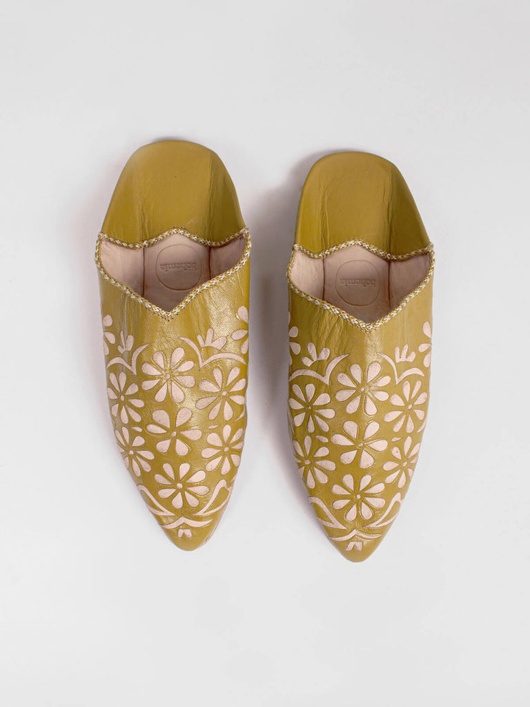 A pair of mustard coloured pointed leather slippers with detailed daisy cut work pattern.