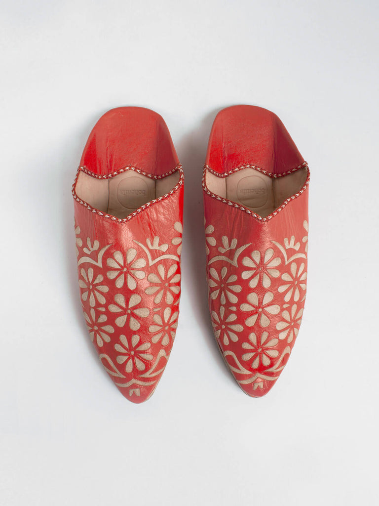 A pair of orange leather Moroccan decorative babouche slippers with a daisy pattern.