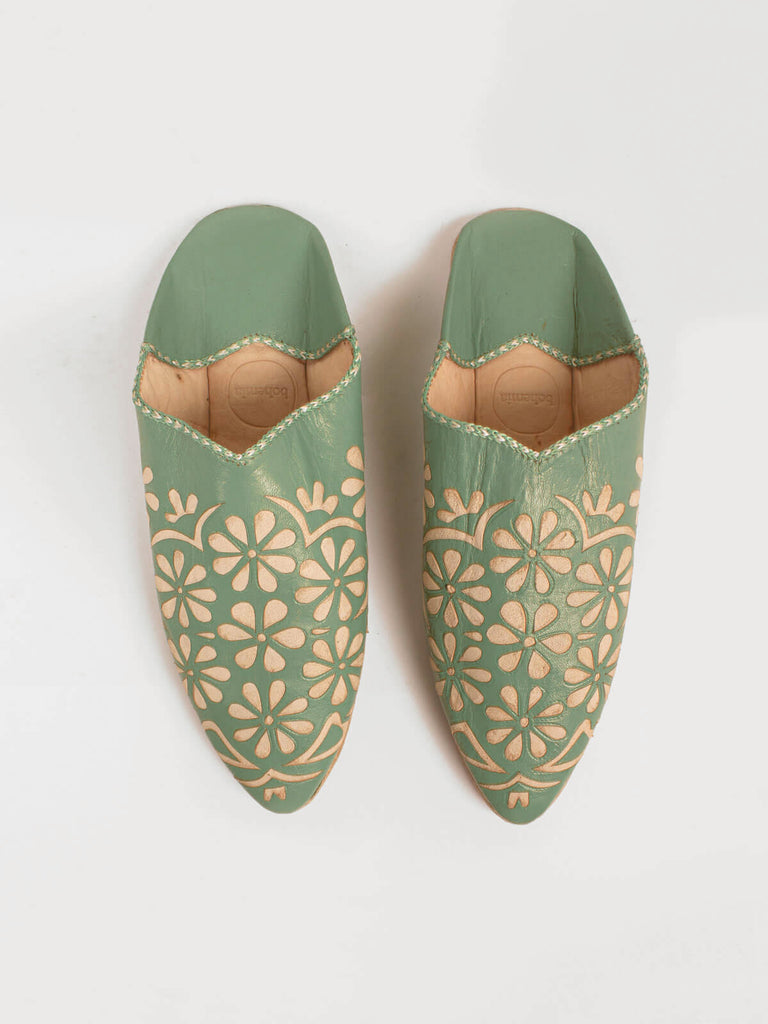 A pair of sage green leather pointed babouche slippers with delicate daisy cut work pattern.