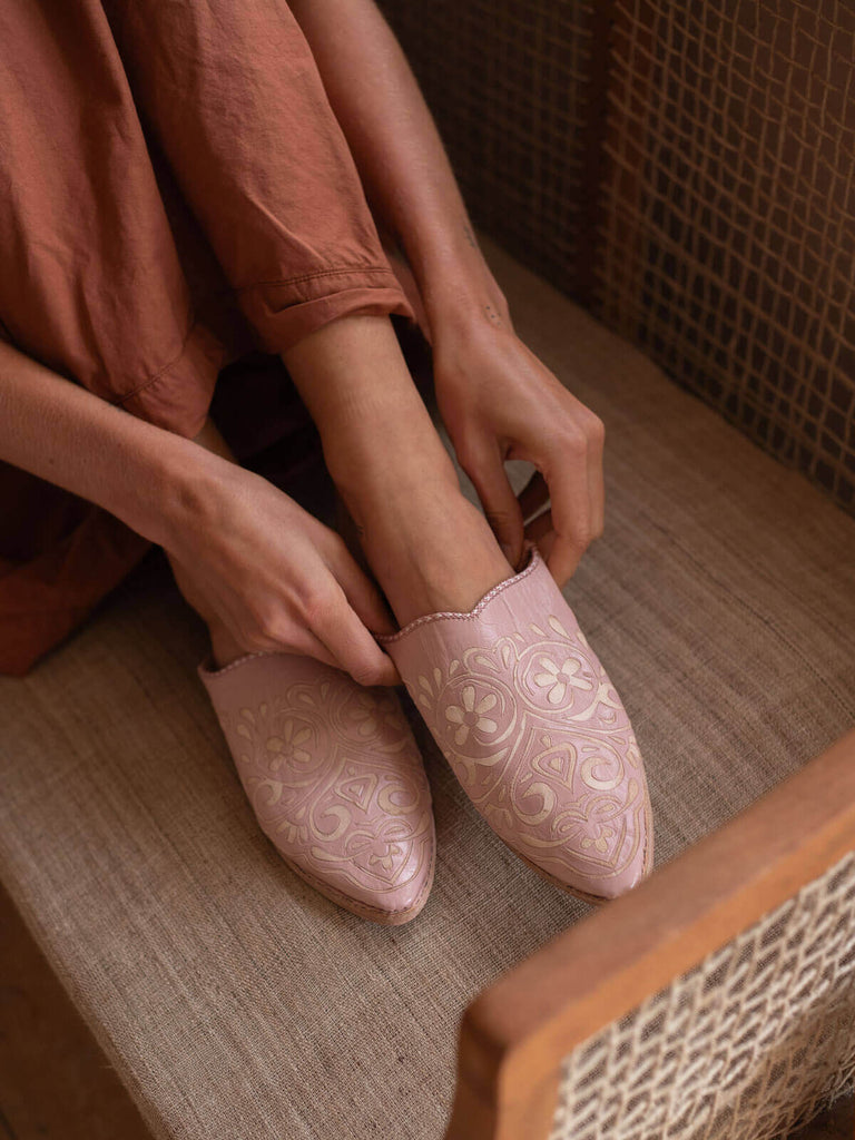 A pair of vintage pink decorative babouche slippers with heart pattern being put on by person in peach dress.
