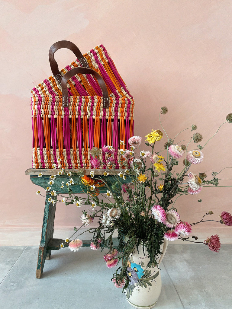 Decorative striped woven reed basket bags with pink and orange stripes, two leather handles and rectangular shape