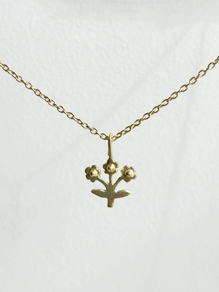 Tiny gold posie necklace featuing a minimalist flower pendant on a fine gold chain