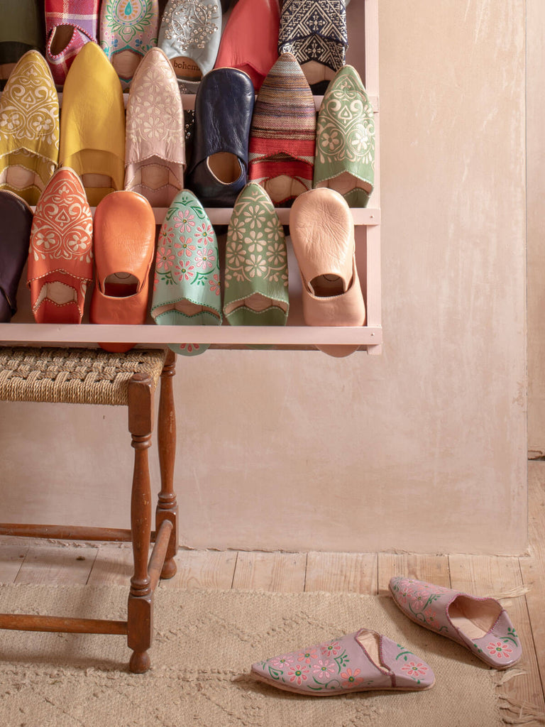 Hand Painted Flower Babouche Slippers on the floor next to a rack filled with different babouche slippers