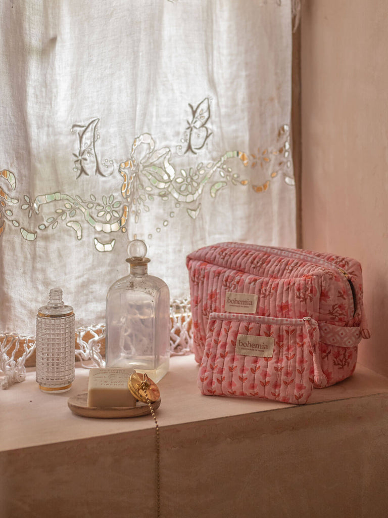A vintage pink quilted washbag and zip pouch on a bathroom windowsill alongside soap and vintage bottles