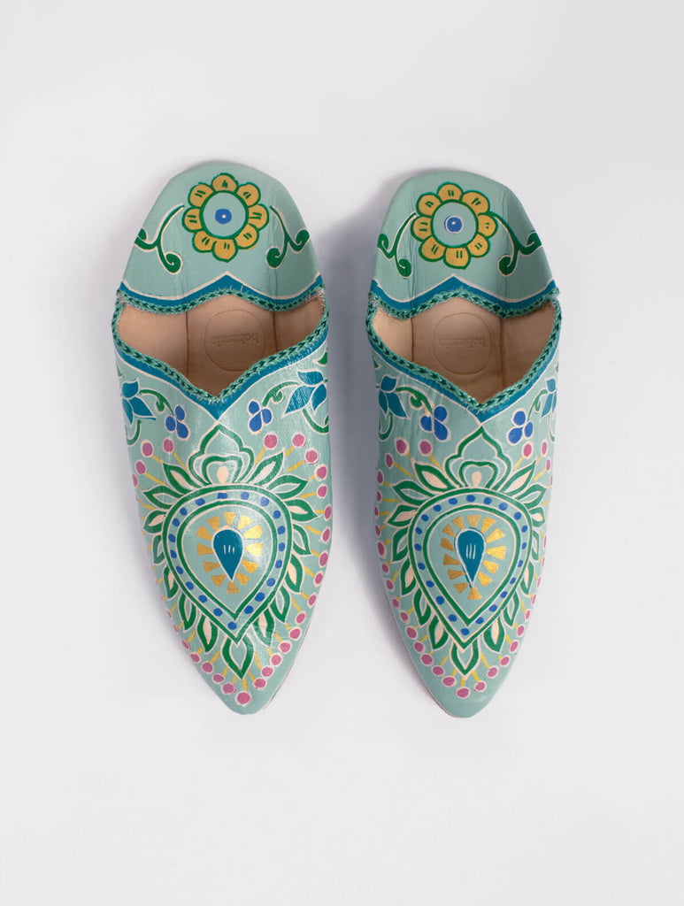 A pair of pointed babouche slippers in a sage green leather with exquisite hand painted, nature inspired elements and golden highlights.