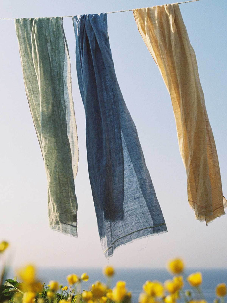 Linen scarves hanging on a washing line by the sea with yellow flowers below